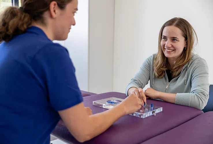Zwei Frauen spielen ein Brettspiel an einem Tisch. Eine Frau lächelt, während die andere konzentriert auf das Spielbrett schaut. Beide wirken entspannt.