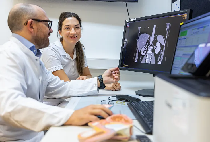 Zwei Personen in medizinischer Kleidung betrachten Röntgenbilder auf einem Monitor. Beide wirken konzentriert und diskutieren die dargestellten Aufnahmen.