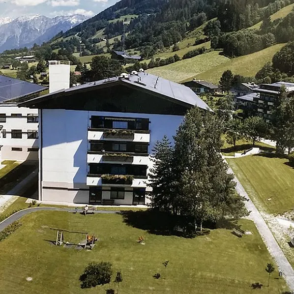 Weitläufige Wohnanlage in alpiner Landschaft mit mehreren modernen Gebäuden, gepflegten Grünflächen und imposanten Bergen im Hintergrund.