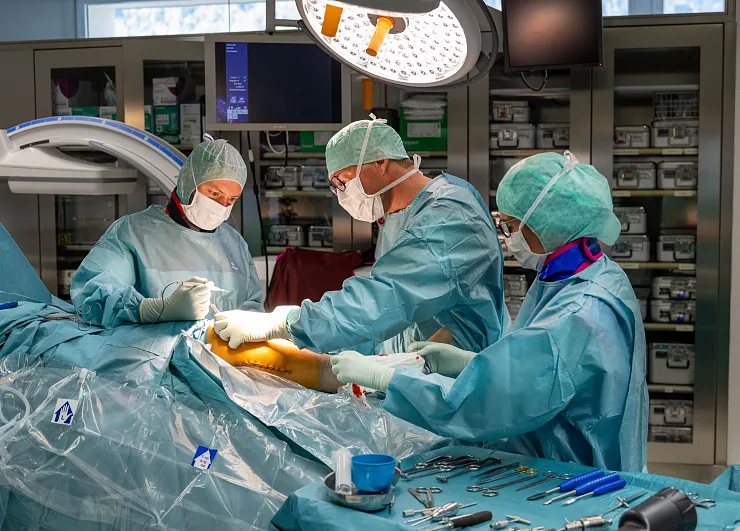 Chirurgen und medizinisches Personal in OP-Kleidung arbeiten konzentriert in einem Operationssaal. Instrumente sind ordentlich auf einem Tisch angeordnet.