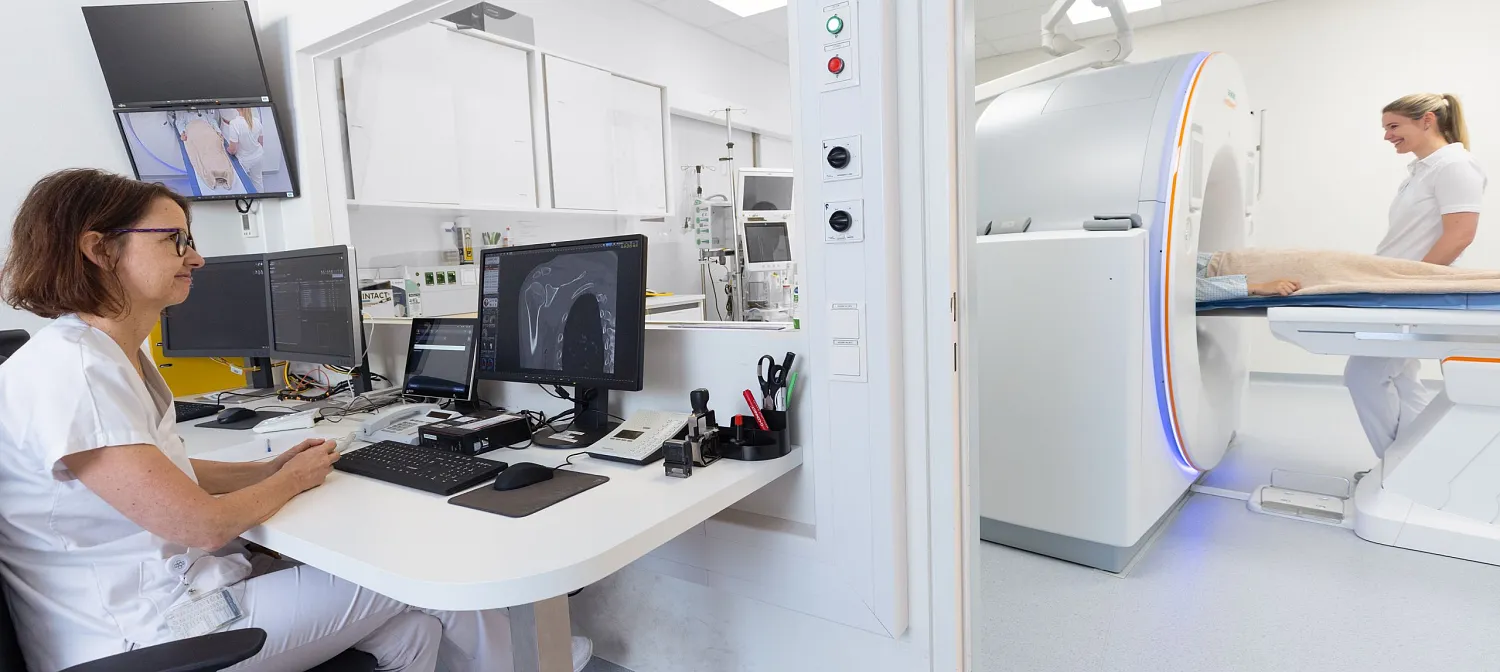 Medizinisches Personal führt eine CT-Untersuchung durch. Eine Person liegt im CT-Scanner, während eine andere am Computer die Untersuchung überwacht.