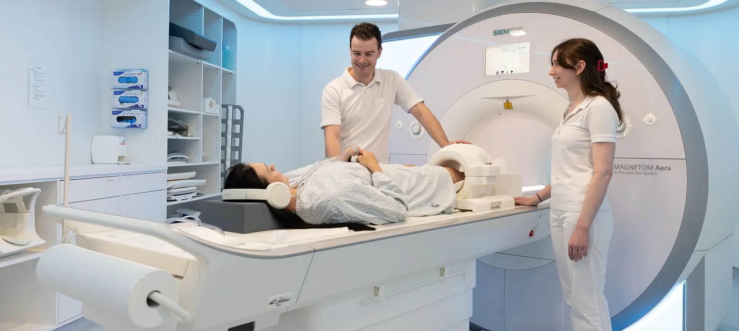 Eine Patientin liegt in einem modernen MRT-Gerät, betreut von zwei medizinischen Fachkräften in einem hellen, sauberen Untersuchungsraum.