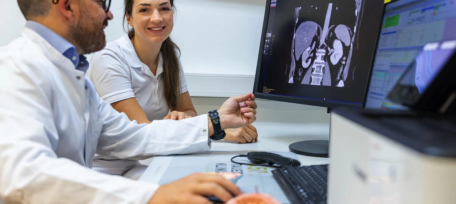 Zwei Personen in medizinischer Kleidung betrachten Röntgenbilder auf einem Monitor. Beide wirken konzentriert und diskutieren die dargestellten Aufnahmen.