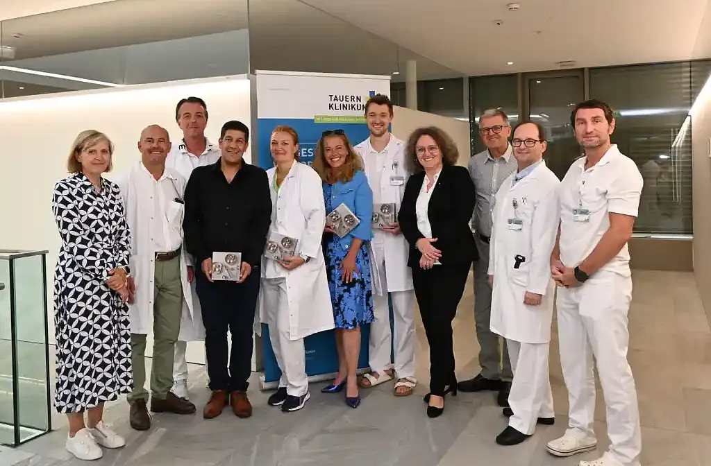 Eine Gruppe von Menschen, teils in weißen medizinischen Kitteln, steht in einem modern gestalteten Innenraum. Sie lächeln und posieren für ein Foto.