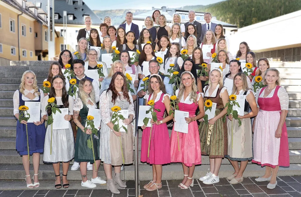 Eine große Gruppe von Menschen in traditioneller Tracht versammelt sich auf einer Treppe. Viele halten Sonnenblumen und einige haben Zertifikate in der Hand.
