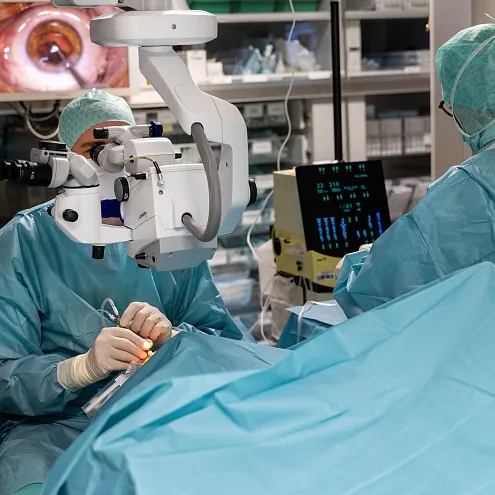 Chirurgische Szene in einem Operationssaal mit medizinischem Personal, das ein modernes Mikroskop und Überwachungsgeräte während eines Eingriffs verwendet.