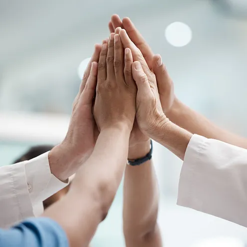 Eine Gruppe von Händen verschiedener Personen in einem kollektiven High-Five. Die Umgebung ist unscharf, was den Fokus auf die Hände legt.