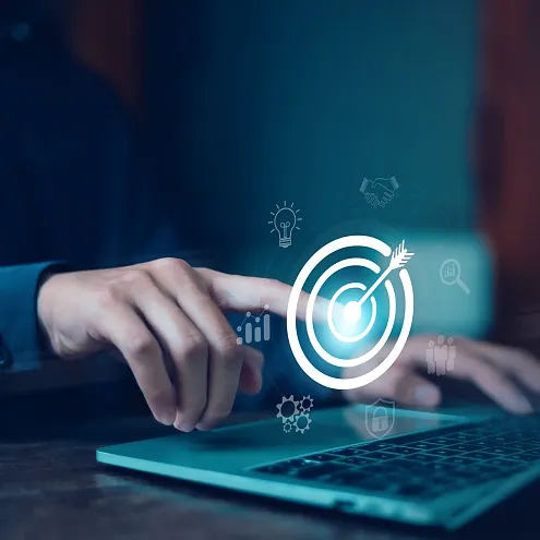 Ein Mensch bedient einen Laptop, während ein digitales Zielscheiben-Symbol auf dem Bildschirm schwebt. Symbole für Ideen und Suche sind ebenfalls sichtbar.