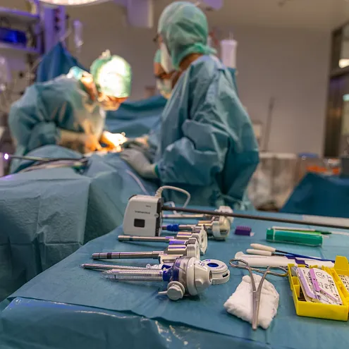 Chirurgisches Team in einem OP-Saal, konzentriert bei der Arbeit. Im Vordergrund sind chirurgische Instrumente und Werkzeuge aufgereiht zu sehen.