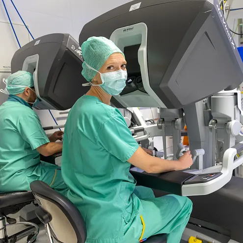 Chirurgen in OP-Kleidung bedienen moderne, robotergesteuerte medizinische Geräte in einem Operationssaal, inmitten von komplexen Maschinen und Monitoren.