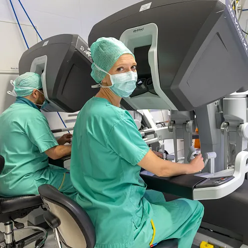 Chirurgen in OP-Kleidung bedienen moderne, robotergesteuerte medizinische Geräte in einem Operationssaal, inmitten von komplexen Maschinen und Monitoren.