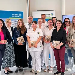 Eine Gruppe von Menschen, darunter medizinisches Personal in Uniform, posiert für ein Foto vor Bannern. Einige halten Auszeichnungen in den Händen.