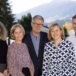 Fünf Personen stehen nebeneinander vor einer Berglandschaft. Sie lächeln in die Kamera, bei sonnigem Wetter und vor herbstlicher Vegetation.
