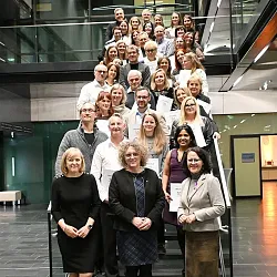 Eine Gruppe von Menschen steht auf einer Treppe und hält Zertifikate. Die Personen lächeln und posieren für das Foto in einem modernen Gebäude.